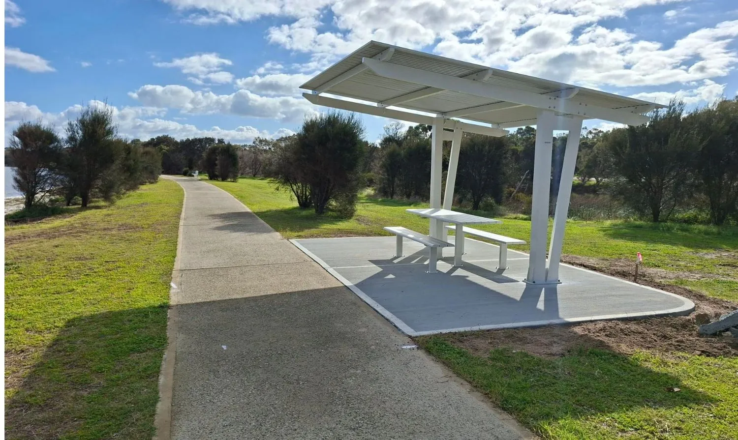 Sheltered bench seat located next to concrete path on water's edge.